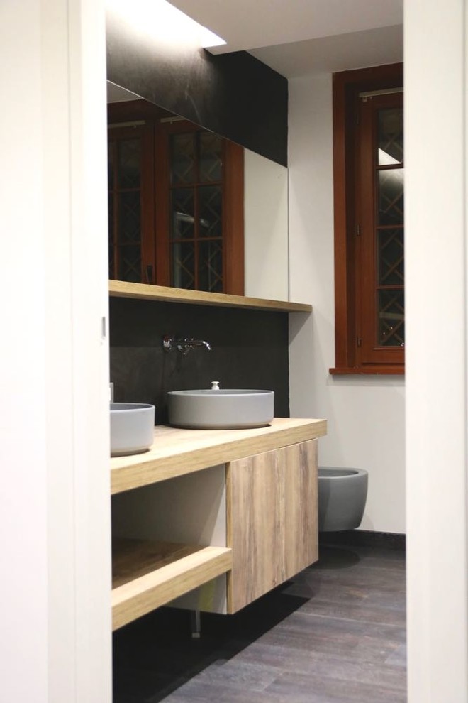 Idées déco pour un grand WC suspendu contemporain en bois clair avec un placard à porte plane, un carrelage noir, un mur noir, un sol en bois brun, une vasque, un plan de toilette en stratifié et un sol marron.