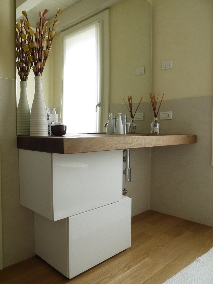 Exemple d'un WC et toilettes tendance de taille moyenne avec un placard à porte vitrée, des portes de placard blanches, un carrelage beige, un mur beige, un sol en bois brun, une grande vasque, un plan de toilette en bois et un sol marron.