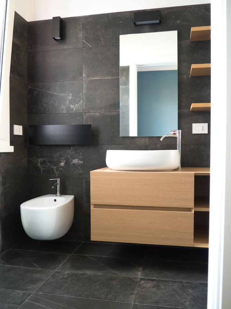 Cette photo montre un petit WC suspendu tendance en bois clair avec un placard à porte affleurante, un carrelage noir, des carreaux de porcelaine, un mur noir, un sol en carrelage de porcelaine, une vasque, un plan de toilette en bois et un sol noir.