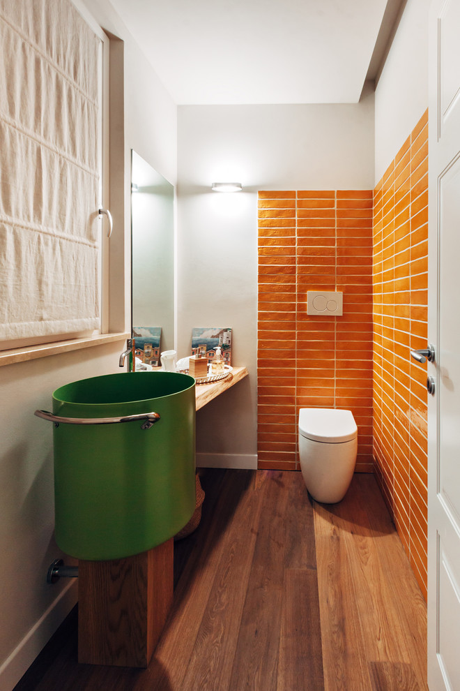 Inredning av ett modernt litet toalett, med orange kakel, keramikplattor, mörkt trägolv, en vägghängd toalettstol, vita väggar och brunt golv