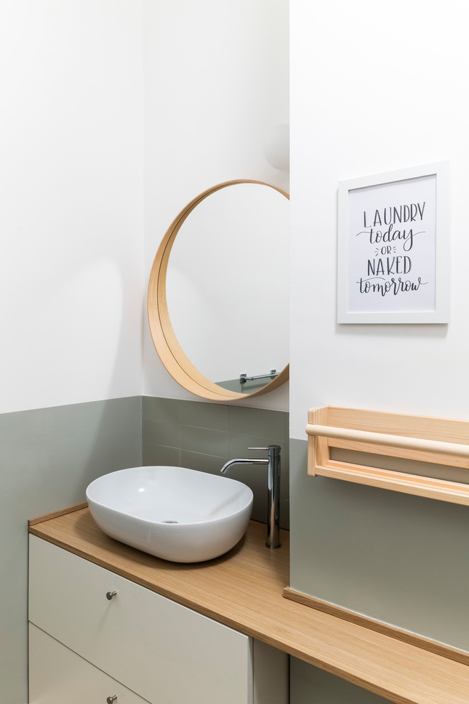 Exempel på ett mellanstort skandinaviskt toalett, med släta luckor, vita skåp, en toalettstol med separat cisternkåpa, grön kakel, porslinskakel, gröna väggar, ljust trägolv, ett fristående handfat och träbänkskiva