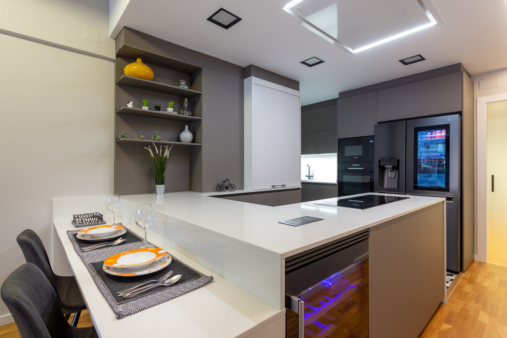 Inspiration for a medium sized contemporary u-shaped kitchen in Barcelona with flat-panel cabinets, black appliances, a breakfast bar, grey cabinets, medium hardwood flooring, brown floors and white worktops.