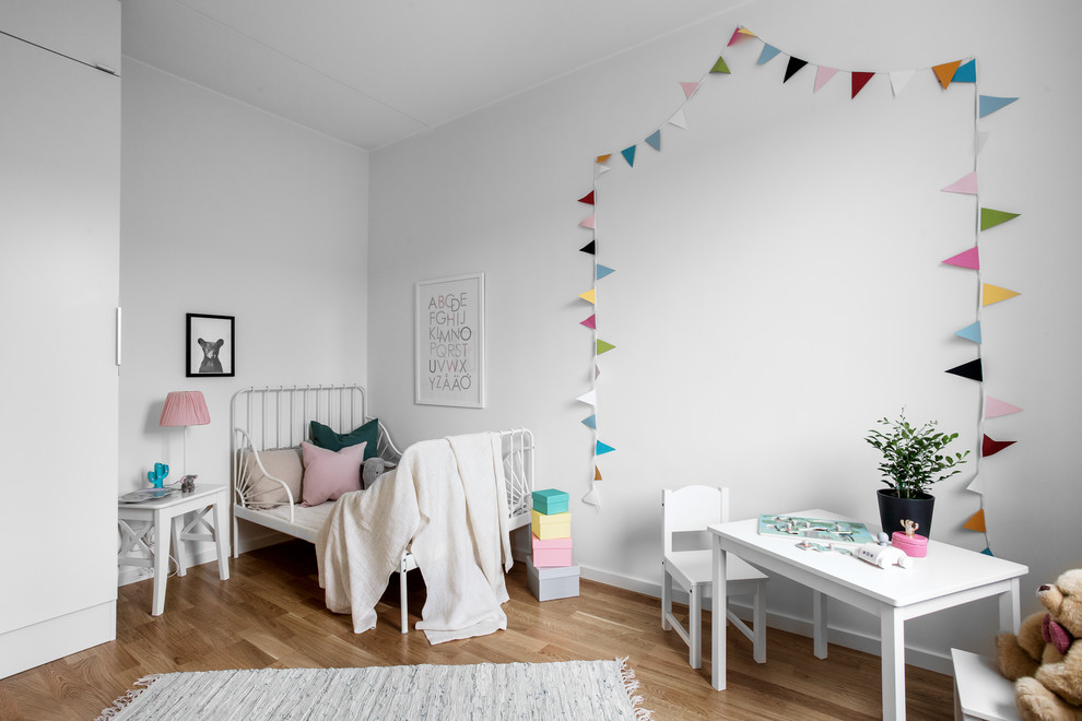 Immagine di una cameretta per bambini da 1 a 3 anni nordica con pareti bianche, pavimento in legno massello medio e pavimento marrone