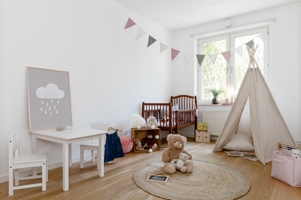 Photo of a medium sized scandi toddler’s room for girls in Stockholm with white walls and light hardwood flooring.