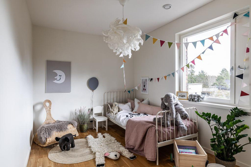 Scandinavian toddler’s room for girls in Stockholm with grey walls and medium hardwood flooring.