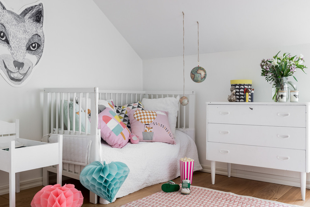 Idée de décoration pour une chambre d'enfant de 1 à 3 ans nordique de taille moyenne avec un mur blanc et un sol en bois brun.