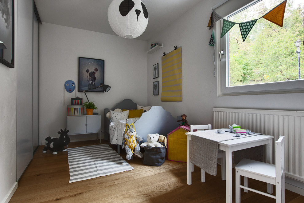 Skandinavisk inredning av ett barnrum, med vita väggar, mellanmörkt trägolv och brunt golv