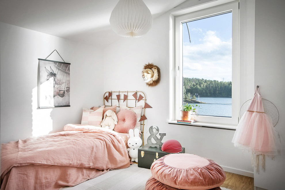 Scandinavian children’s room for girls in Stockholm with white walls, medium hardwood flooring and brown floors.