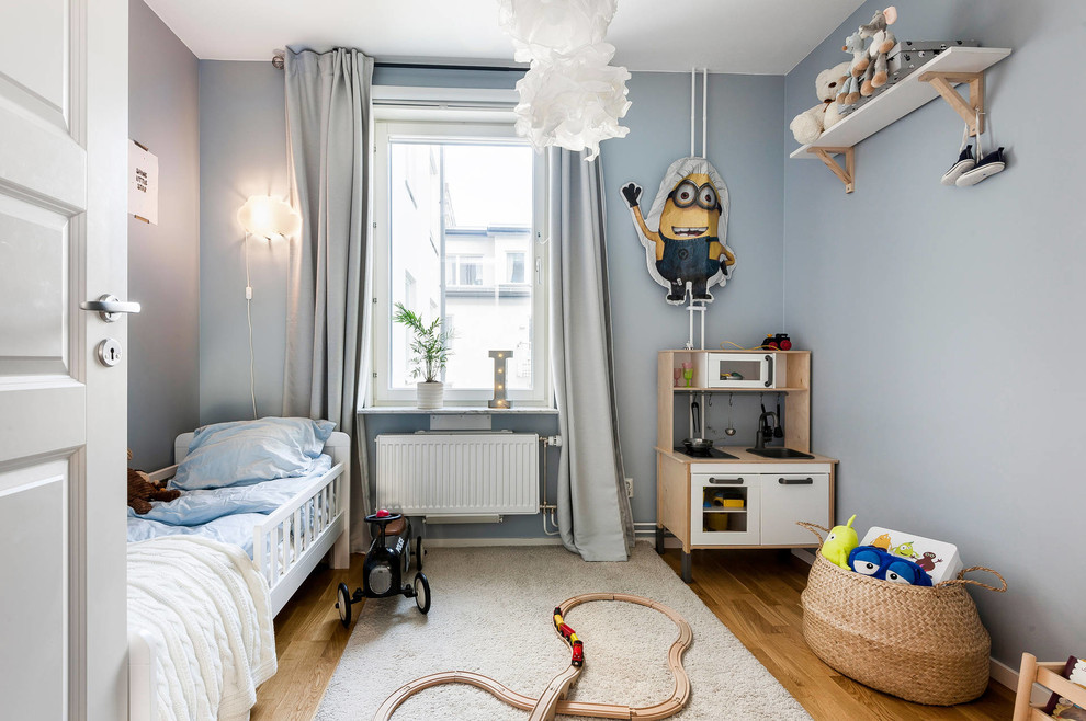 This is an example of a scandinavian kids' bedroom in Stockholm with blue walls, medium hardwood flooring, brown floors and feature lighting.