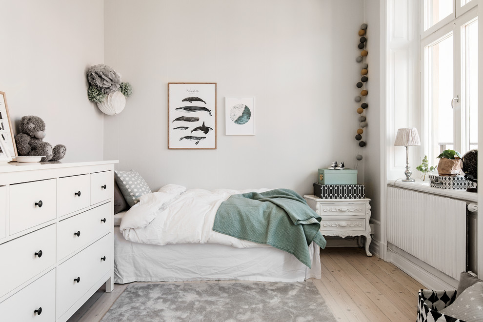 This is an example of a medium sized scandi gender neutral children’s room in Stockholm with white walls, light hardwood flooring and beige floors.