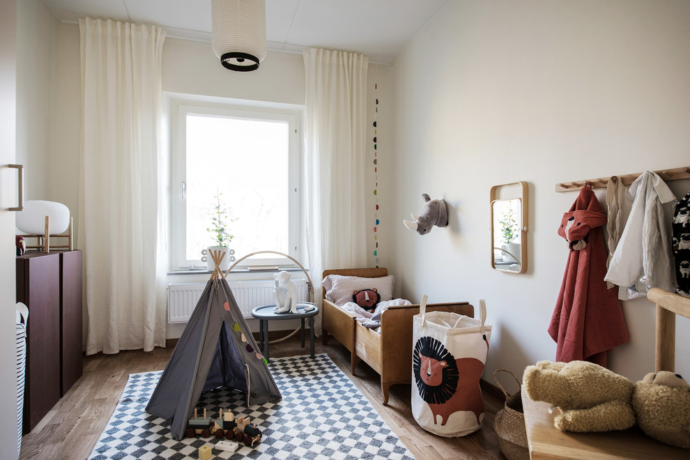 Photo of a scandi gender neutral toddler’s room in Gothenburg with white walls and medium hardwood flooring.