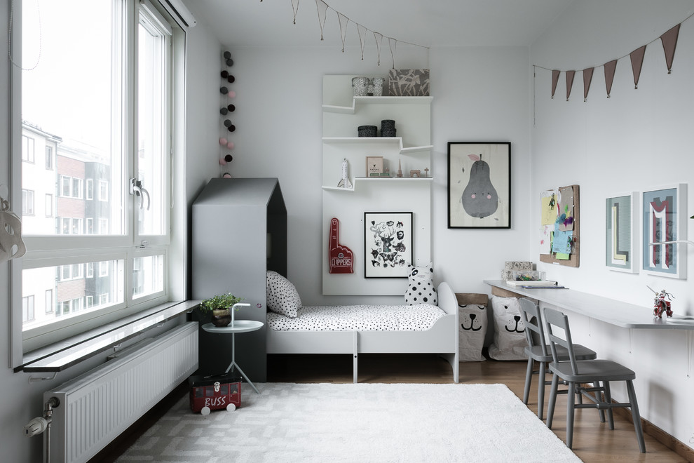 Bild på ett mellanstort nordiskt könsneutralt barnrum kombinerat med sovrum och för 4-10-åringar, med vita väggar, mellanmörkt trägolv och brunt golv