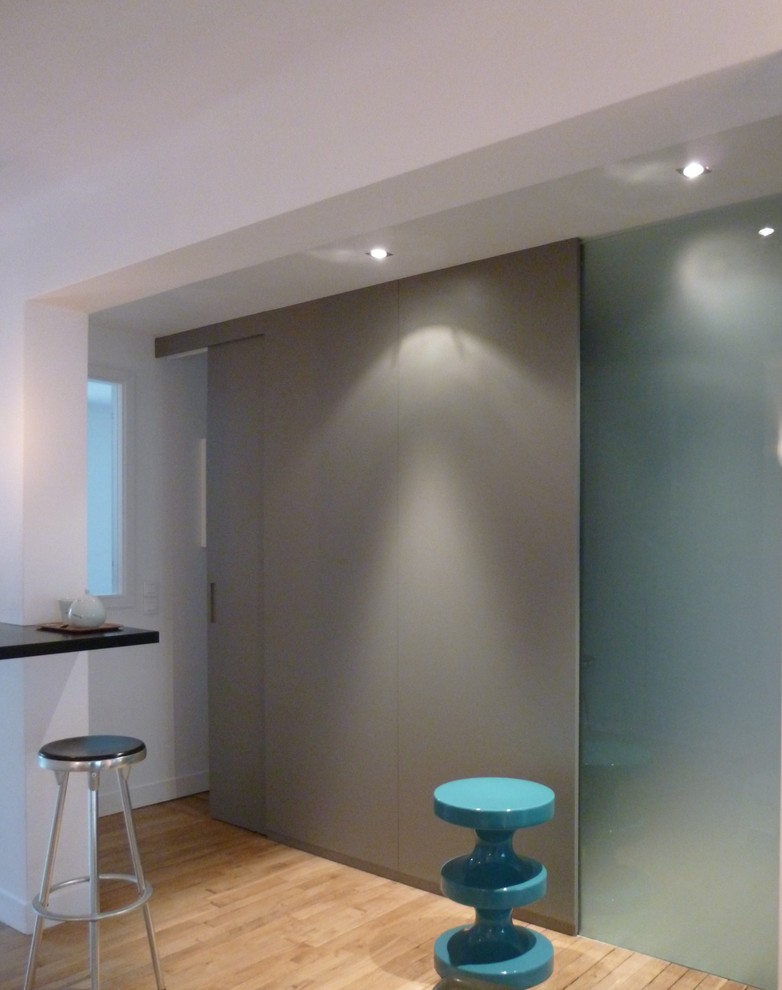 Photo of a medium sized contemporary u-shaped breakfast bar in Paris with glass-front cabinets, grey cabinets, granite worktops, white splashback, light hardwood flooring and beige floors.