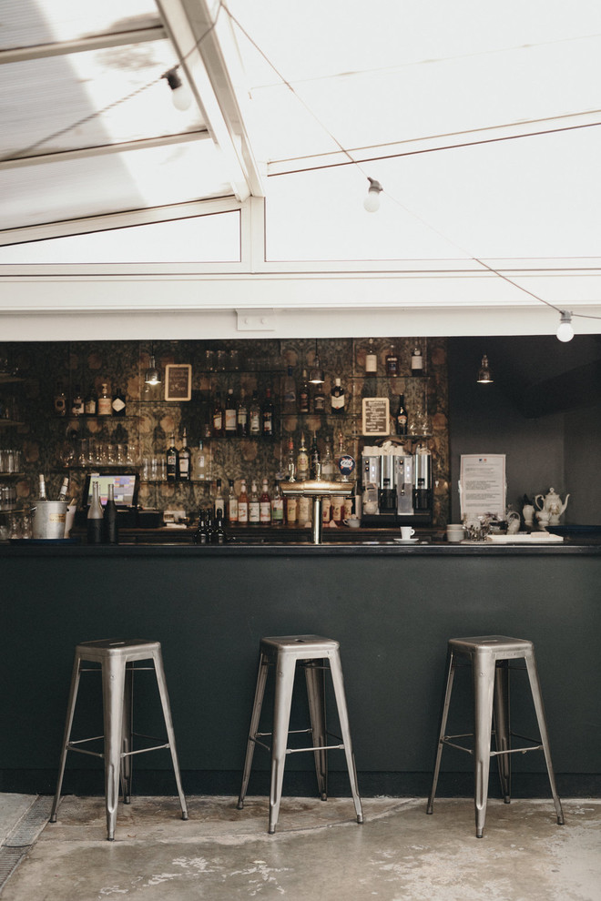 Imagen de bar en casa con barra de bar en L ecléctico con fregadero bajoencimera, armarios abiertos, encimera de madera y suelo de cemento