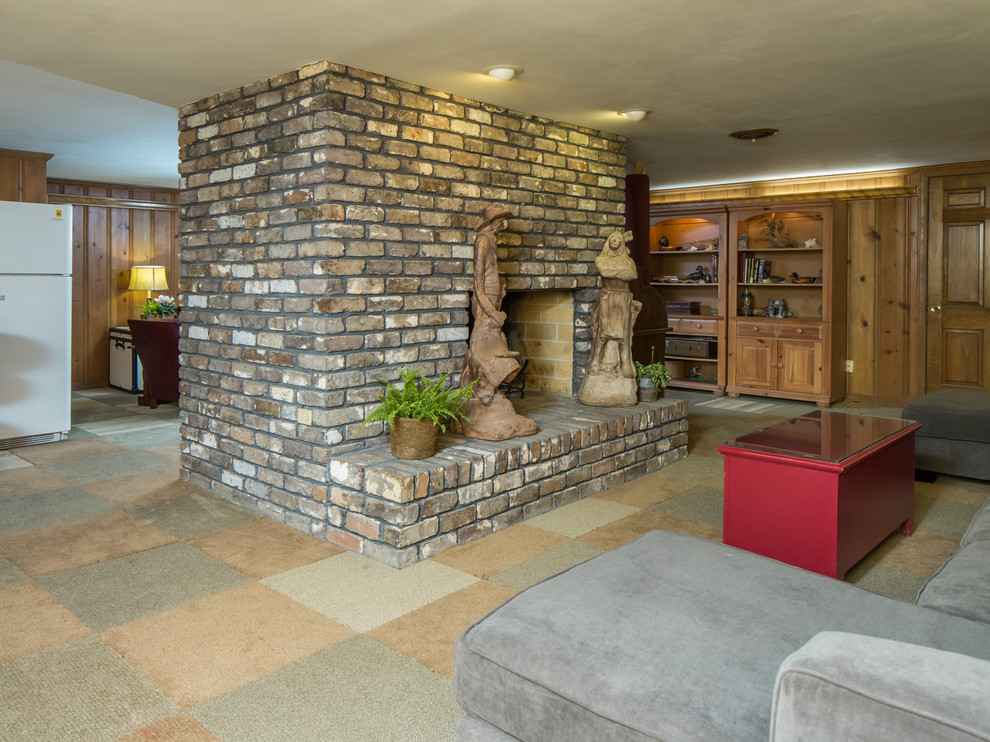 Cette image montre un grand sous-sol vintage enterré avec un mur marron, moquette, une cheminée standard et un manteau de cheminée en brique.
