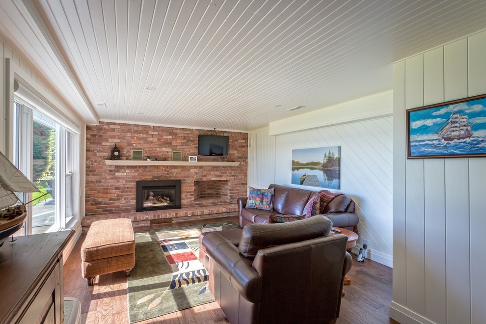 Aménagement d'un petit sous-sol classique donnant sur l'extérieur avec un mur blanc, un sol en bois brun, une cheminée standard et un manteau de cheminée en brique.