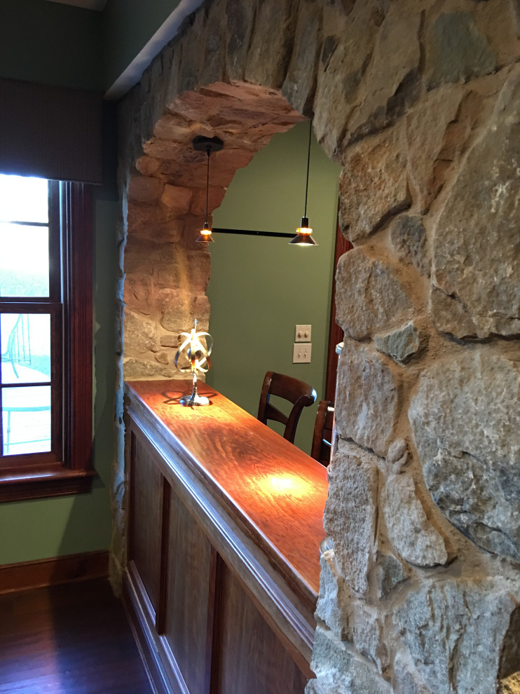 Ejemplo de sótano con puerta tradicional grande con paredes verdes, suelo de madera oscura, todas las chimeneas, marco de chimenea de piedra y suelo marrón