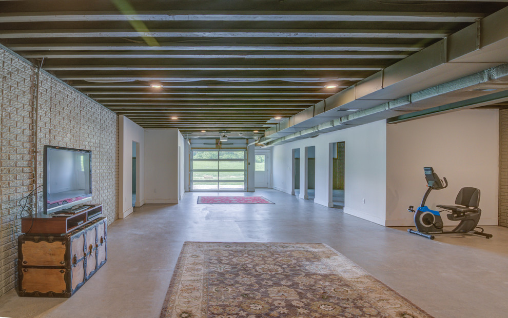 Cette image montre un grand sous-sol design donnant sur l'extérieur avec un mur blanc, sol en béton ciré et un sol gris.