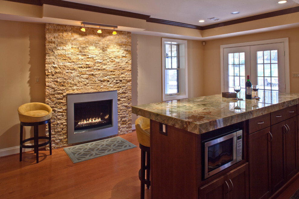 Exemple d'un grand sous-sol tendance donnant sur l'extérieur avec un mur beige, un sol en bois brun, une cheminée standard et un manteau de cheminée en pierre.