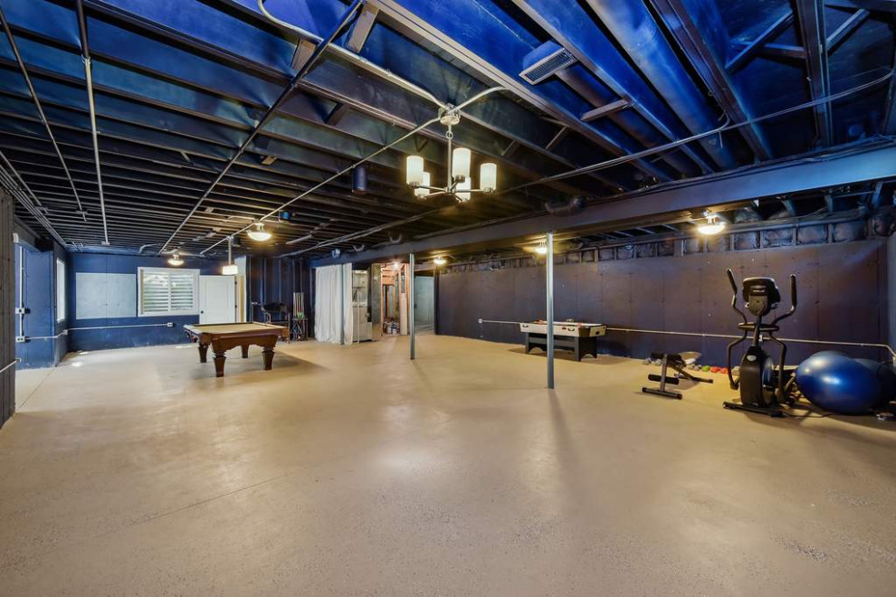На фото: подземный, большой подвал в стиле неоклассика (современная классика) с игровой комнатой, фиолетовыми стенами, бетонным полом, бежевым полом и балками на потолке