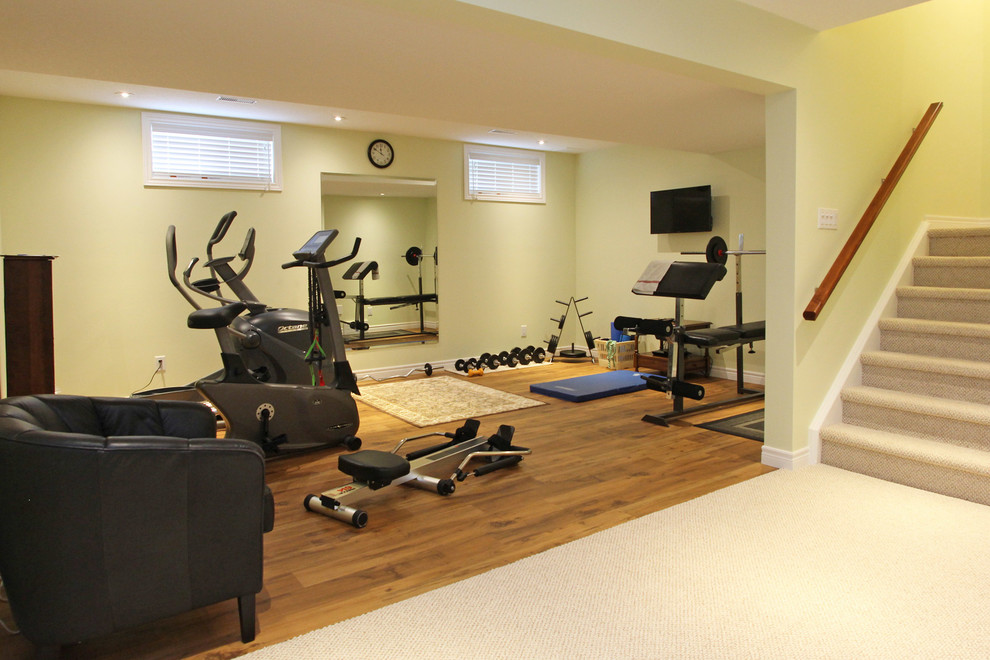 Großer Klassischer Fitnessraum mit gelber Wandfarbe, braunem Holzboden und braunem Boden in Sonstige