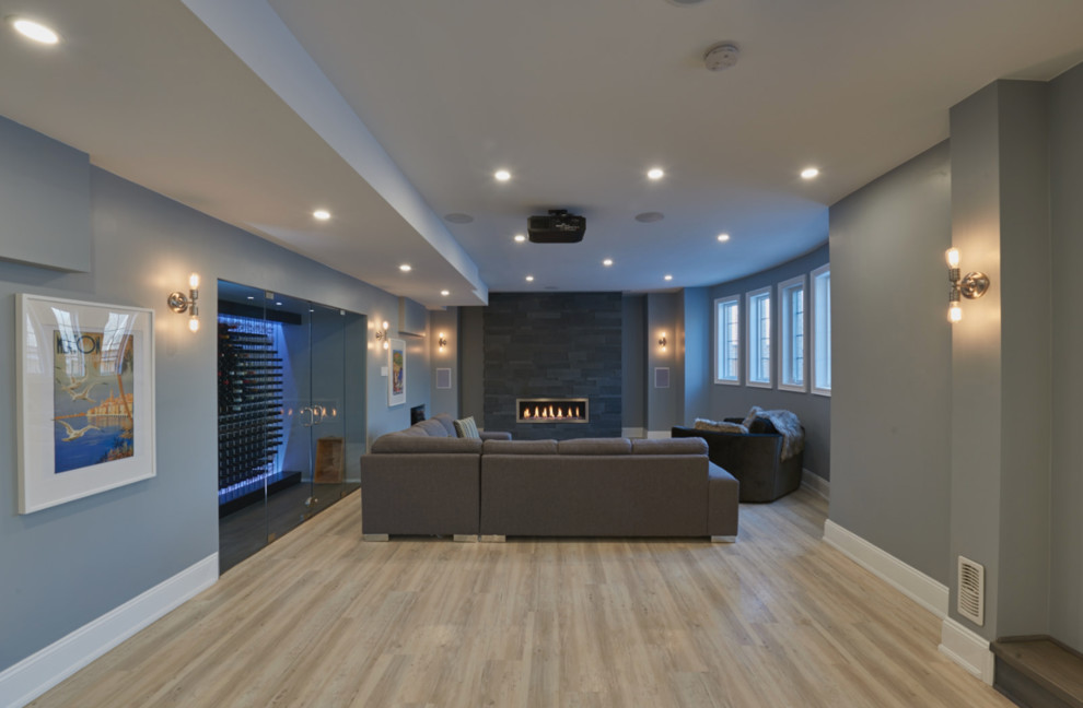 Traditional walk-out basement in Toronto with grey walls, light hardwood flooring, a ribbon fireplace and a stone fireplace surround.
