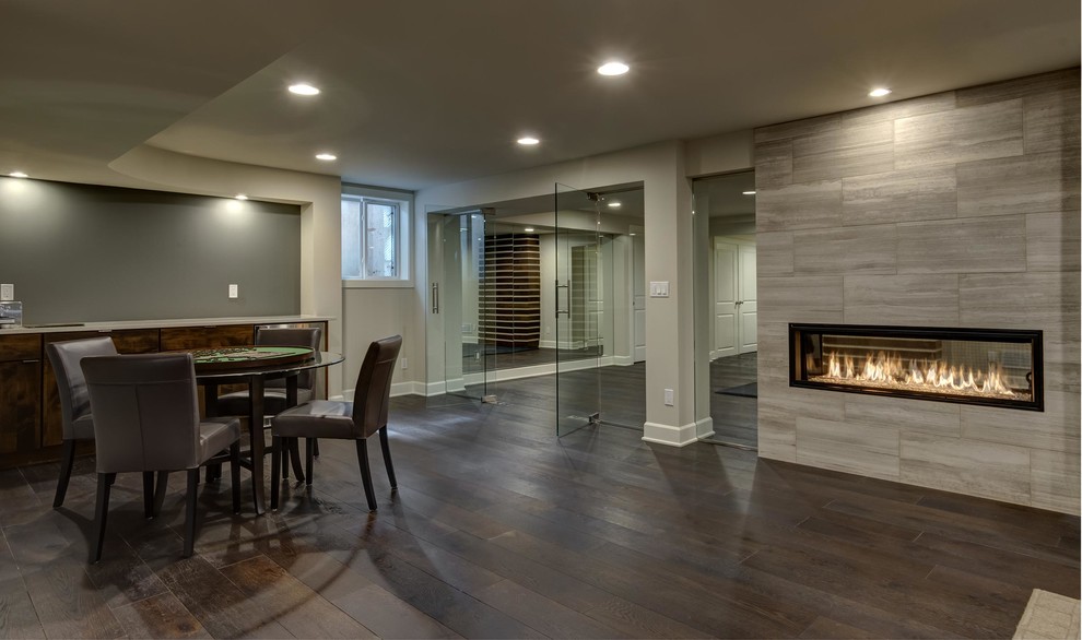 This is an example of an expansive contemporary look-out basement in Denver with grey walls, dark hardwood flooring, a ribbon fireplace, a tiled fireplace surround and brown floors.