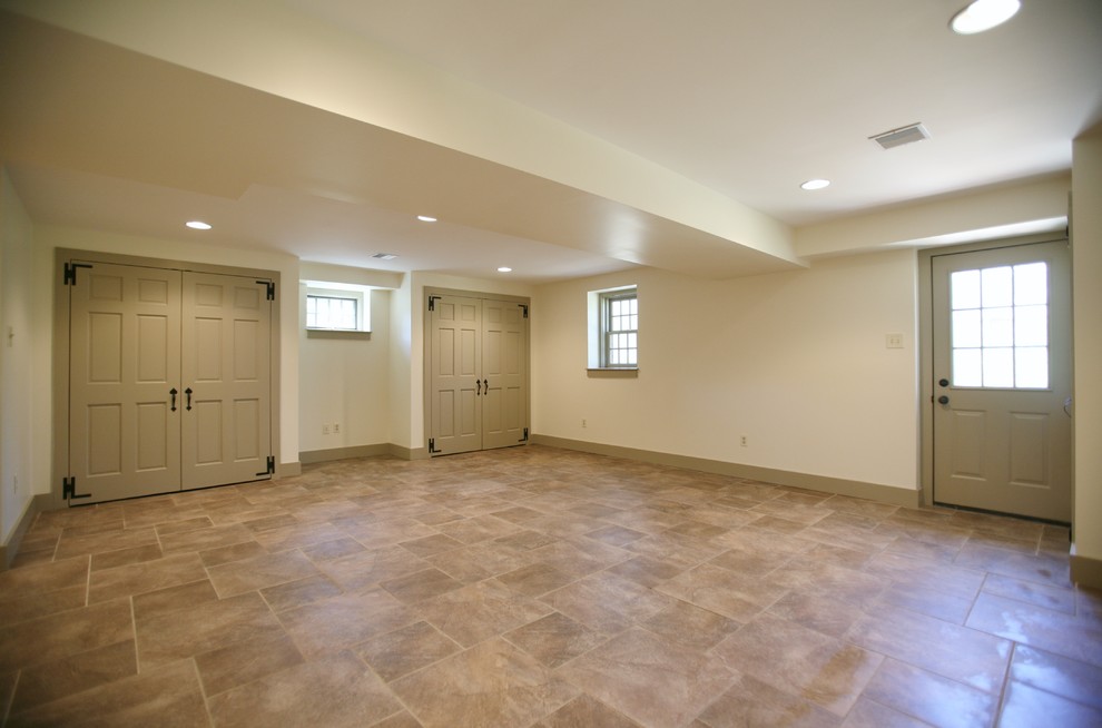 Cette image montre un grand sous-sol traditionnel donnant sur l'extérieur avec un mur beige, aucune cheminée et un sol en linoléum.