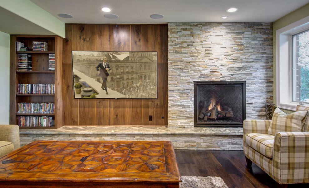 Cette photo montre un grand sous-sol chic donnant sur l'extérieur avec un mur vert, un sol en bois brun, une cheminée standard, un manteau de cheminée en pierre et un sol marron.