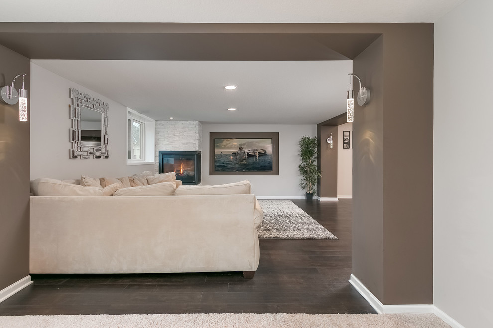 Example of a large transitional walk-out dark wood floor and brown floor basement design in Minneapolis with gray walls, a corner fireplace and a tile fireplace