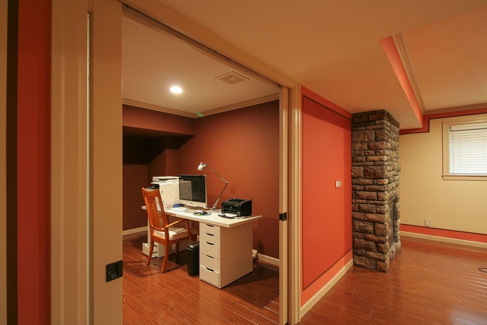 Photo of a medium sized traditional fully buried basement in Vancouver with orange walls, medium hardwood flooring, a standard fireplace, a stone fireplace surround and brown floors.