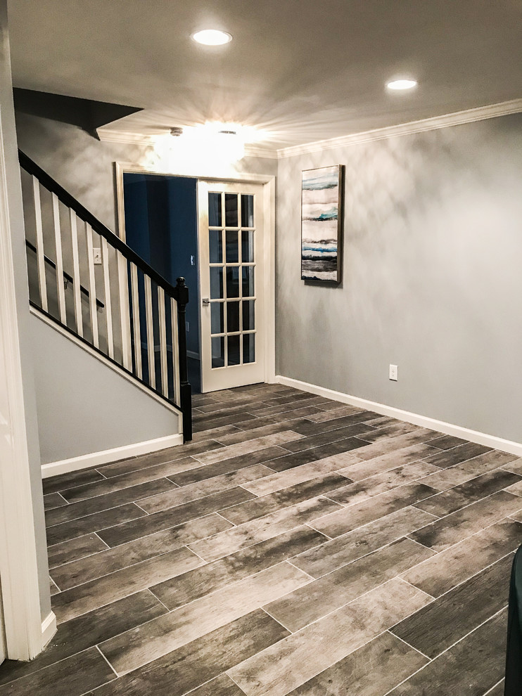 This is an example of a large traditional walk-out basement in DC Metro with grey walls, ceramic flooring, a standard fireplace, a brick fireplace surround and grey floors.