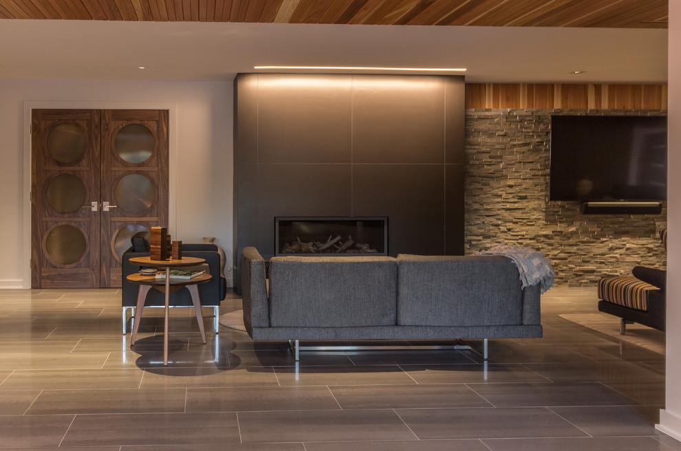 Photo of a large contemporary walk-out basement with white walls, porcelain flooring, a standard fireplace, a tiled fireplace surround and grey floors.