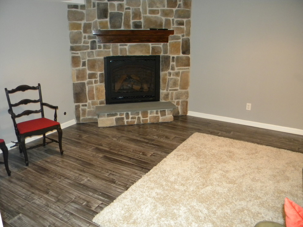 This is an example of a rustic walk-out basement in Philadelphia with grey walls, dark hardwood flooring, a standard fireplace and a stone fireplace surround.