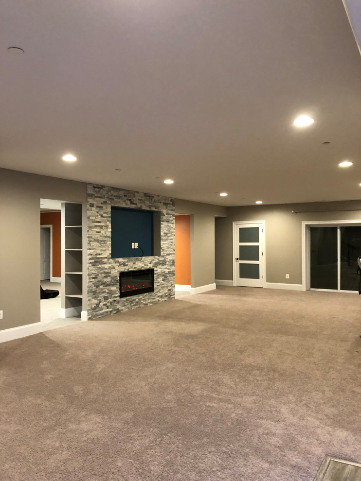 This is an example of a large modern look-out basement with grey walls, carpet, a ribbon fireplace, a stone fireplace surround and beige floors.