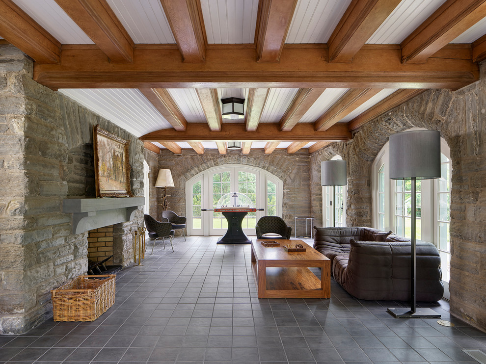 Cette image montre un grand sous-sol traditionnel donnant sur l'extérieur avec un mur gris, un sol en carrelage de porcelaine, une cheminée standard, un manteau de cheminée en pierre et un sol gris.