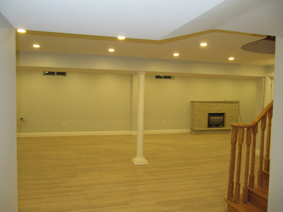 Idée de décoration pour un grand sous-sol minimaliste enterré avec un mur gris, sol en stratifié, une cheminée standard, un manteau de cheminée en carrelage et un sol gris.