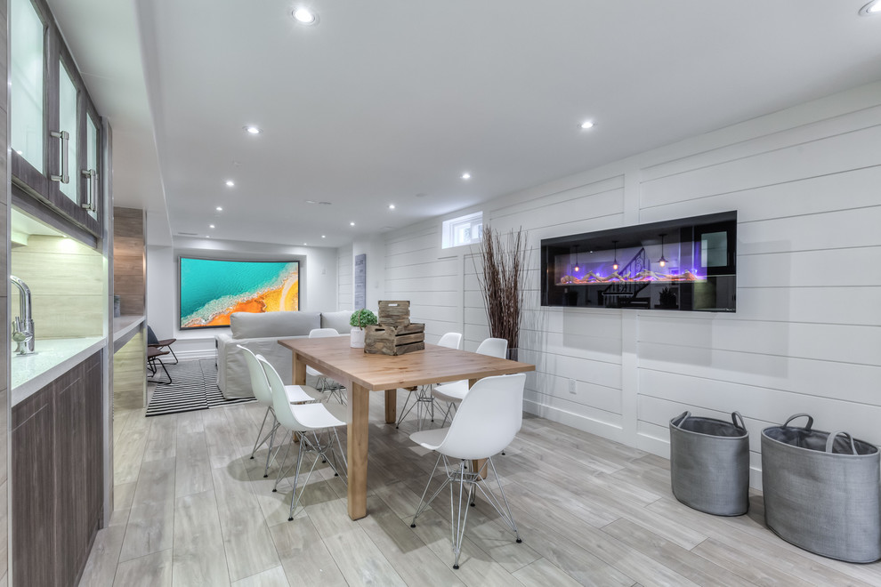 Example of a large beach style walk-out laminate floor basement design in Toronto with white walls and a ribbon fireplace