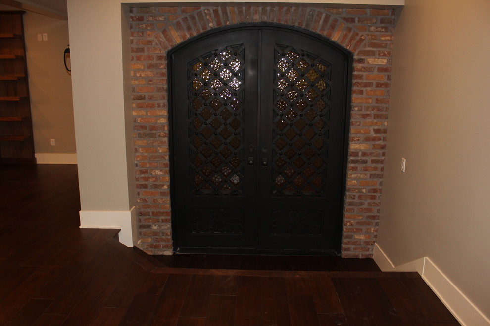 Cette image montre un grand sous-sol traditionnel donnant sur l'extérieur avec un mur gris, un sol en bois brun, une cheminée standard et un manteau de cheminée en pierre.
