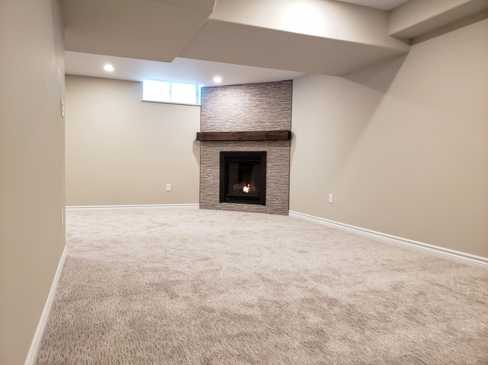 Inspiration for a medium sized traditional look-out basement in Toronto with beige walls, carpet, a corner fireplace, a tiled fireplace surround and grey floors.