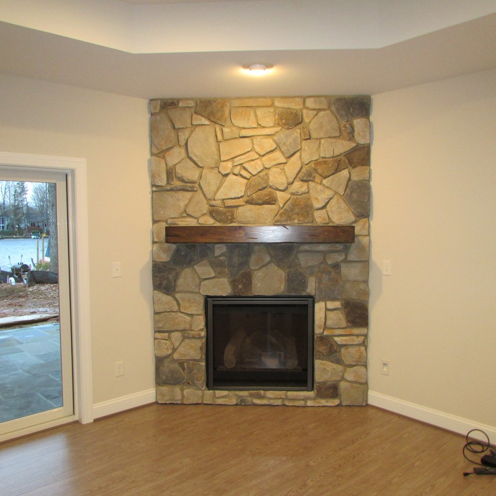 Cette image montre un grand sous-sol craftsman donnant sur l'extérieur avec un mur beige, sol en stratifié, une cheminée d'angle, un manteau de cheminée en pierre et un sol gris.