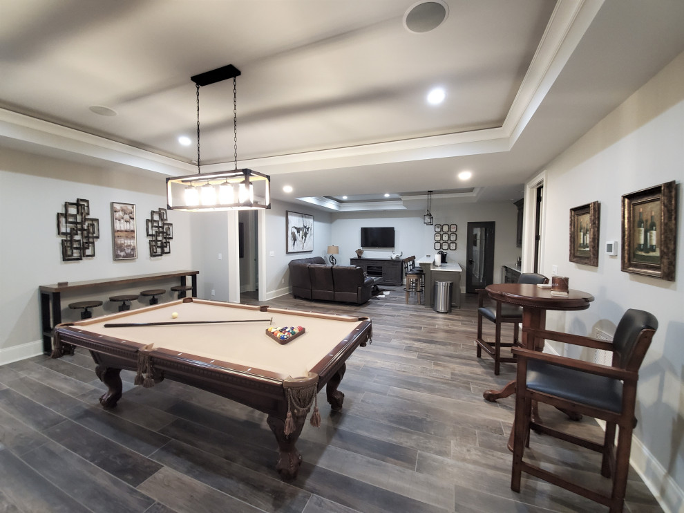 Example of a medium tone wood floor, multicolored floor and tray ceiling basement game room design in Charlotte with gray walls
