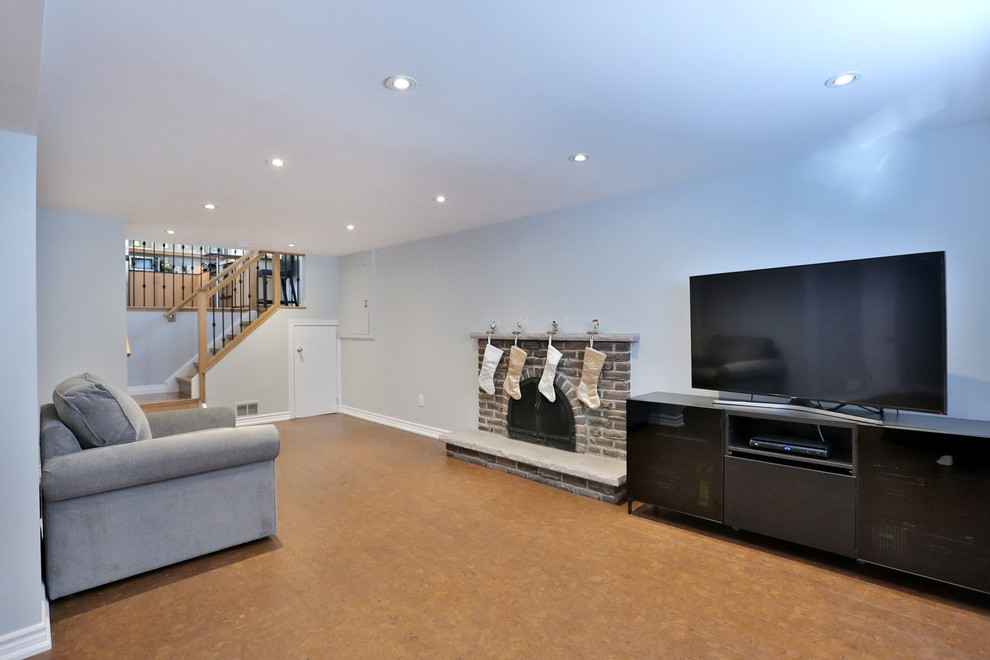 Cette photo montre un sous-sol moderne de taille moyenne avec un mur gris, un sol en liège, une cheminée standard et un manteau de cheminée en pierre.