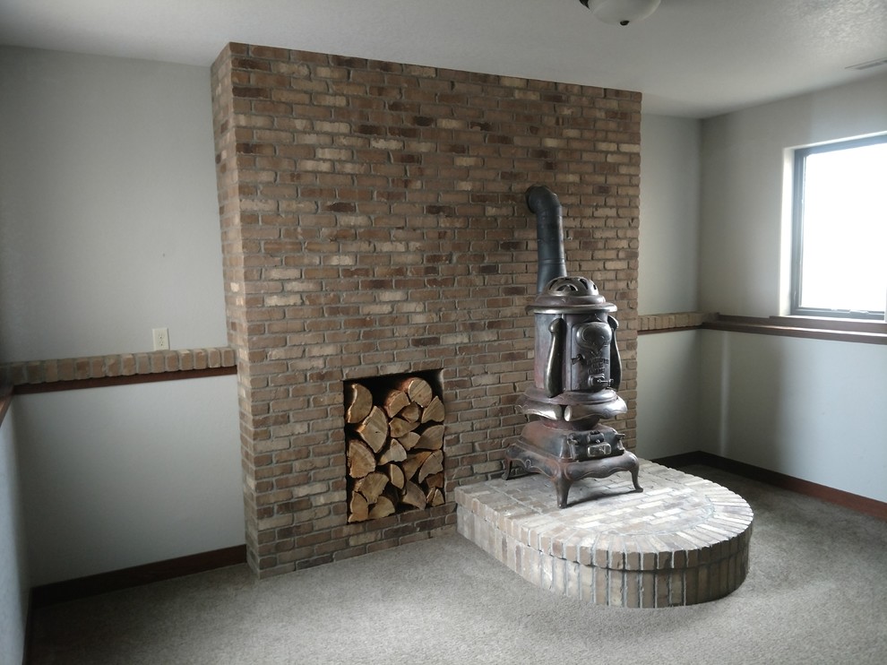 Photo of a medium sized traditional look-out basement in Other with white walls, carpet, a wood burning stove, a brick fireplace surround and grey floors.