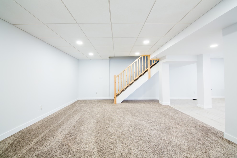 Cette image montre un très grand sous-sol design semi-enterré avec un mur bleu, un sol en vinyl et un sol beige.