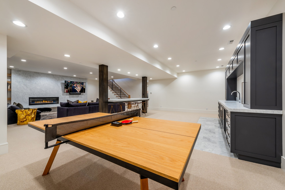 This is an example of a large contemporary fully buried basement in Salt Lake City with a home bar, white walls, carpet, a standard fireplace, a stone fireplace surround and beige floors.
