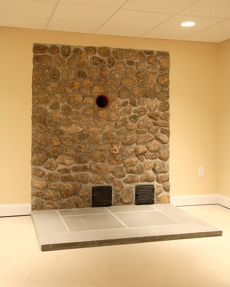 Modelo de sótano en el subsuelo clásico de tamaño medio con paredes beige, moqueta, estufa de leña, marco de chimenea de piedra y suelo beige