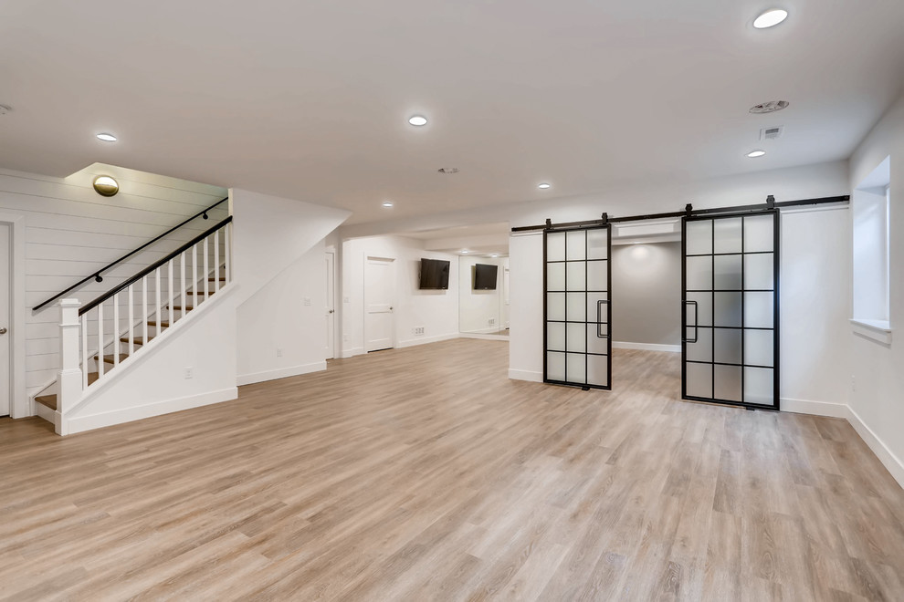 Large fully buried basement in Denver with white walls, light hardwood flooring, no fireplace and beige floors.