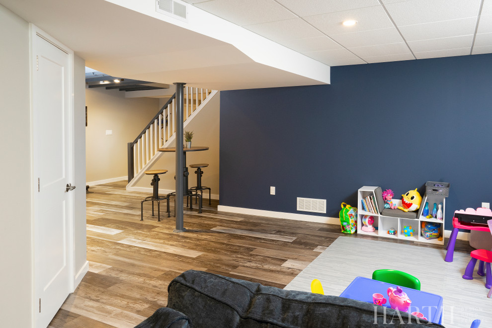 This is an example of a medium sized urban fully buried basement in Philadelphia with a home bar, beige walls, laminate floors, multi-coloured floors and exposed beams.