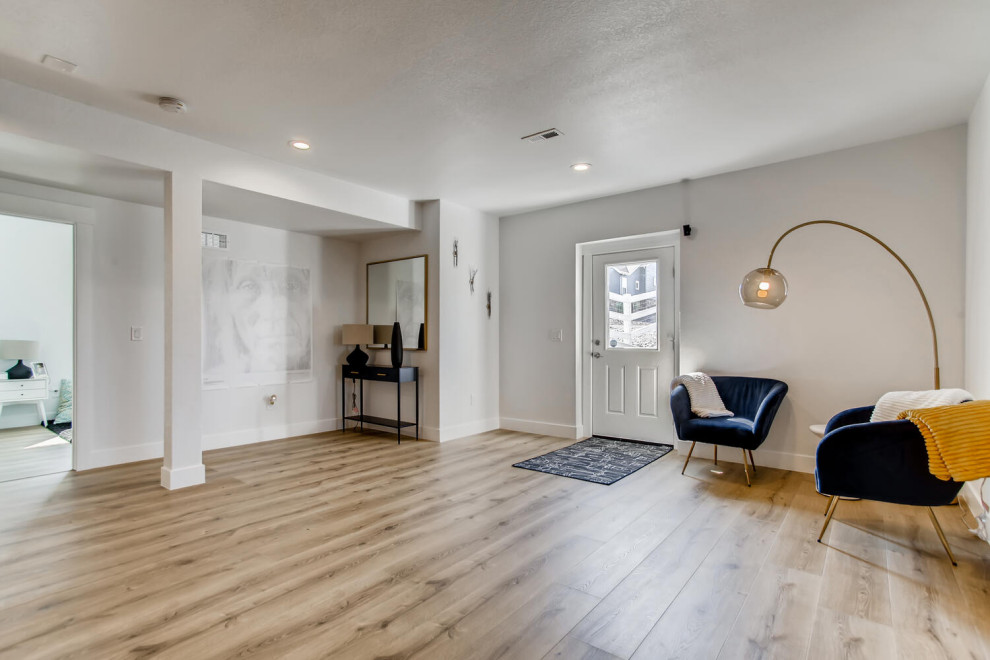 Cette image montre un grand sous-sol design donnant sur l'extérieur avec un bar de salon, un mur gris, un sol en vinyl et un sol marron.